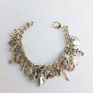 May include: A silver charm bracelet with a variety of charms, including a key, a star, a heart, a feather, a bottle, a sunflower, and a hand. The bracelet is made of a thick chain.