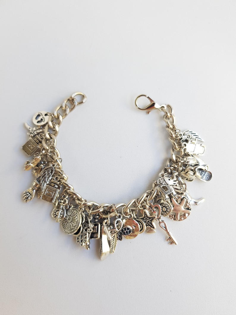 May include: A silver charm bracelet with a variety of charms, including a key, a star, a heart, a feather, a bottle, a sunflower, and a hand. The bracelet is made of a thick chain.