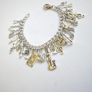 May include: A silver charm bracelet with a variety of music-themed charms, including a guitar, a microphone, a cassette tape, and musical notes.