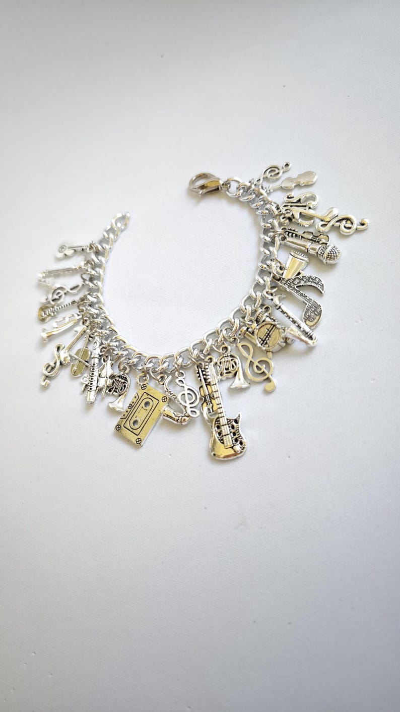 May include: A silver charm bracelet with a variety of music-themed charms, including a guitar, a microphone, a cassette tape, and musical notes.