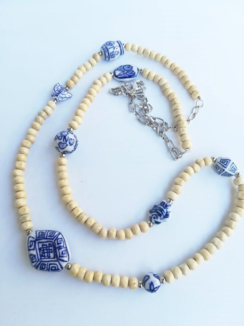 May include: A long necklace made of light brown wooden beads with blue and white porcelain beads featuring Chinese characters and floral designs. The necklace has a silver chain clasp.
