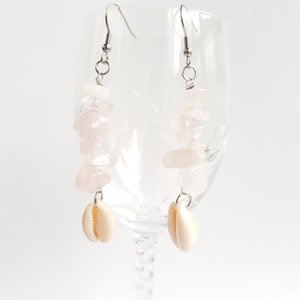 May include: A pair of earrings with pink rose quartz stones and white shell charms hanging from silver hooks.