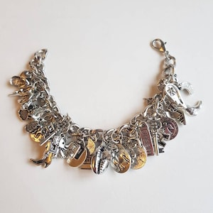 May include: A silver charm bracelet with a variety of charms, including a key, a heart, a star, a moon, a feather, a book, a seashell, and a small elephant. The bracelet is on a white background.