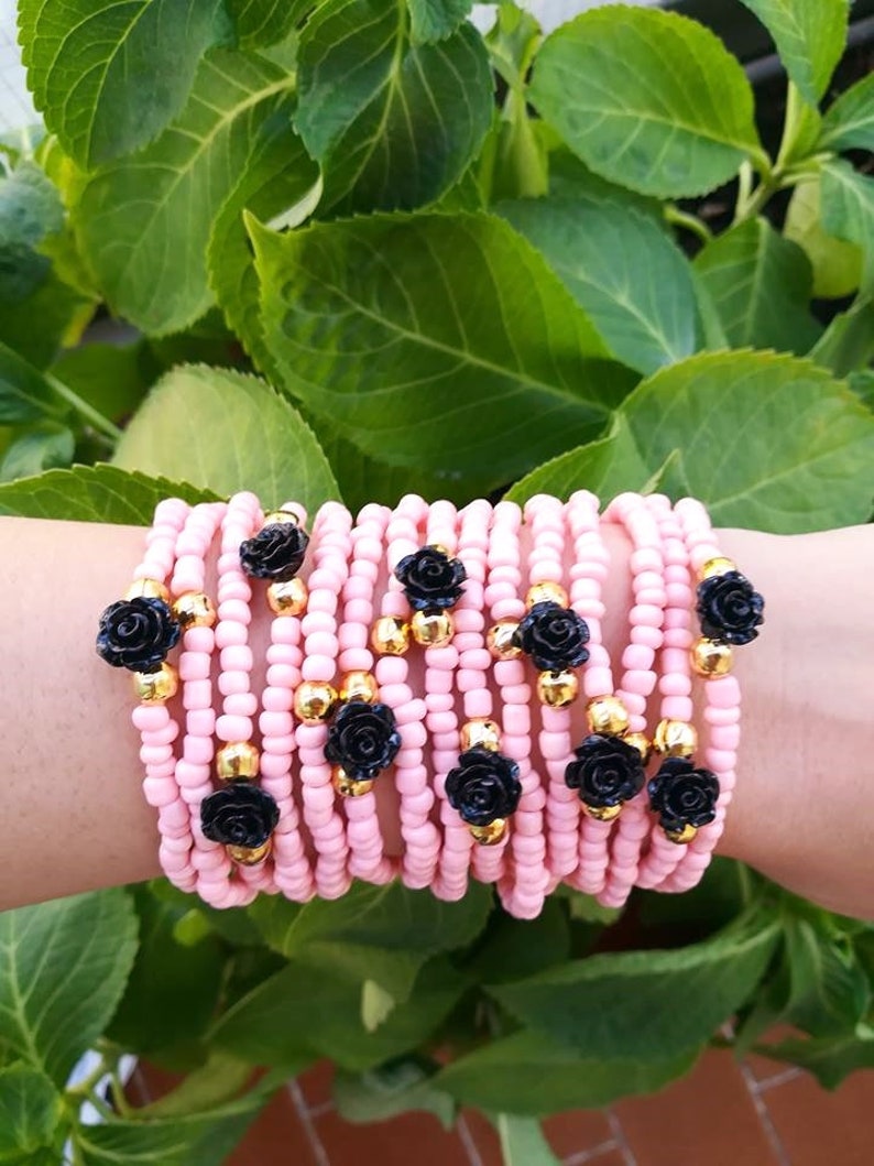 Op de afbeelding: Een stapel roze kralenarmbanden met zwarte roosaccenten en gouden kralen.