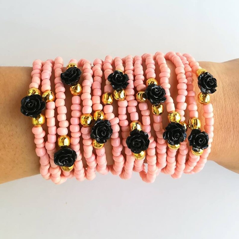 Op de afbeelding: Een stapel roze kralenarmbanden met zwarte roosaccenten. Elke armband heeft een enkele zwarte roosbedel.
