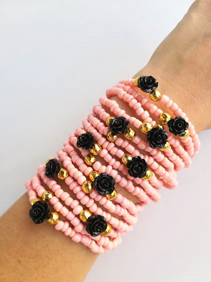 Op de afbeelding: Een stapel roze kralenarmbanden met zwarte roosaccenten en gouden kralen.