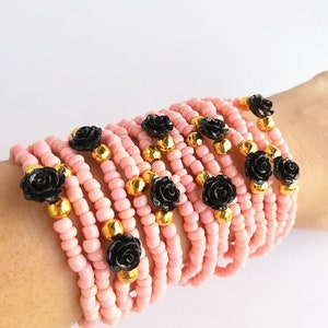 Op de afbeelding: Een stapel roze kralenarmbanden met zwarte roosaccenten en gouden kralen.