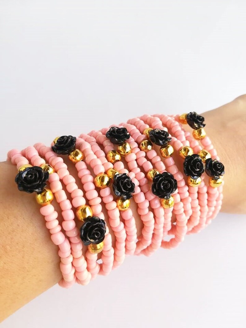 Op de afbeelding: Een stapel roze kralenarmbanden met zwarte roosaccenten en gouden kralen.