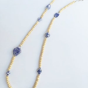 May include: A long necklace made of light brown wooden beads with blue and white porcelain accents. The porcelain accents feature intricate designs.