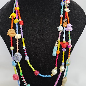 May include: Multi-strand beaded necklace with colorful beads and charms, including a red heart, a blue fish, a yellow star, a white elephant, a white Buddha, a blue and white turtle, a red Mickey Mouse head, a blue tassel, a white pearl, and a yellow flower.