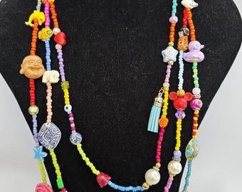 May include: Multi-strand beaded necklace with colorful beads and charms, including a red heart, a blue fish, a yellow star, a white elephant, a white Buddha, a blue and white turtle, a red Mickey Mouse head, a blue tassel, a white pearl, and a yellow flower.
