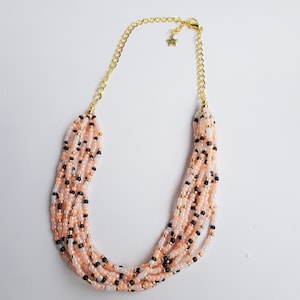 May include: Multi-strand necklace made of small pink, white and black beads. The necklace has a gold chain closure with a star charm.