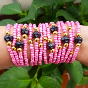Op de afbeelding: Een stapel roze en gouden kralenarmbanden met zwarte schedelbedels.
