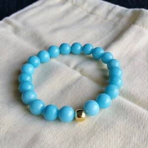 May include: A light blue beaded bracelet with a gold bead accent.
