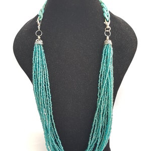 Può includere: Una lunga collana di perline turchesi con chiusure argentate. La collana è esposta su un manichino nero.