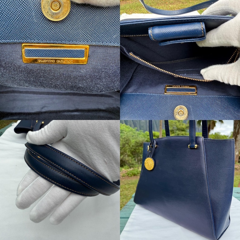 Op de afbeelding: Een marineblauwe Valentino Garavani handtas met goudkleurige hardware. De tas heeft een gestructureerd ontwerp, handvatten aan de bovenkant en een gouden logo-embleem. De binnenkant heeft een ritsvak en een magnetische sluiting.