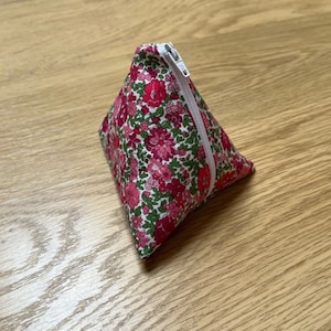 May include: A small triangular zippered pouch with a pink and green floral print. The pouch is made of fabric and has a white zipper.