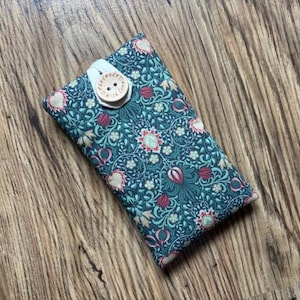 May include: A teal floral patterned phone case with a wooden button closure. The fabric design features flowers and leaves in teal, red, and cream. The wooden button is stamped with the words "handmade with love". The case is rectangular in shape.