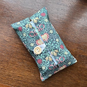 May include: A rectangular tissue holder with a teal, red, and beige floral pattern. It has a white ribbon closure with a wooden button. The fabric displays a detailed botanical design.