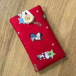 May include: A rectangular red fabric item with a Snoopy cartoon print, white stars, and the word "HUGS". A wooden button with the words "handmade with love" is attached with a white ribbon and blue star.