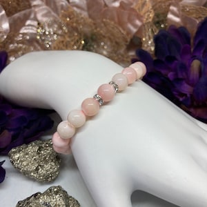 Könnte beinhalten: Ein rosa-weißes Armband mit silbernen Akzenten. Das Armband besteht aus runden Perlen und hat ein elastisches Band.