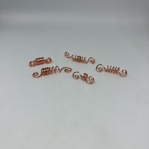 May include: Five copper-colored wire components with a spiral and coil design. The components are arranged on a white surface. The wire has a shiny finish and appears to be handmade, suitable for jewelry making or craft projects.