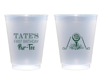 May include: Two frosted plastic cups with green text and graphics. One cup says "Tate's First Birthday Par-Tee". The other cup has a golf ball with the letters "T.B." inside and two golf clubs.