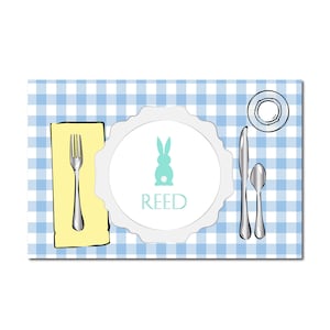 May include: An Easter-themed place setting with a blue and white checkered tablecloth. A white plate with a scalloped edge features a teal bunny and the name "REED". Silverware, a napkin, and a small plate complete the setting.
