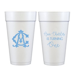 May include: Two white foam cups with blue text and designs. One cup says "Ann Charles is turning One" and the other has a blue monogram.