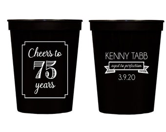 May include: Two black plastic cups with white text. One cup says "Cheers to 75 years". The other cup says "Kenny Tabb aged to perfection 3.9.20".