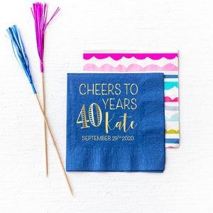May include: Blue paper napkins with gold foil lettering. The text reads "Cheers to 40 Years Kate September 29th 2020".