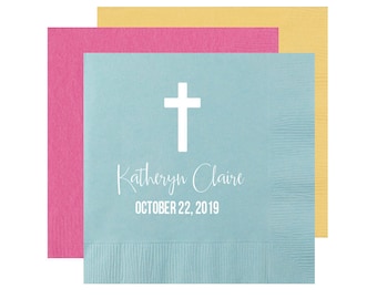 May include: Stack of three pastel colored napkins with a white cross and the text "Kathryn Claire OCTOBER 22, 2019" printed on the top napkin.