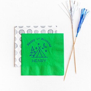 May include: Green paper napkin with a blue design of a tent, trees, stars, and a crescent moon. The text "Happy 1st Birthday HENRY" is printed around the design.