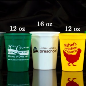 May include: A collection of ten plastic cups in various sizes and colors, including orange, red, silver, green, white, and yellow. The cups are printed with different logos and text, including "Casino Royale", "Cavendor Auto Family", "Ciroc", "Hill Country", "Highlands Preschool", "Ethel's Chicken Shack", "Burgerfl", "Recana", and "Fisherman's Jack's". The cups are arranged in a row from largest to smallest, with the largest cup being 32 ounces and the smallest cup being 12 ounces.