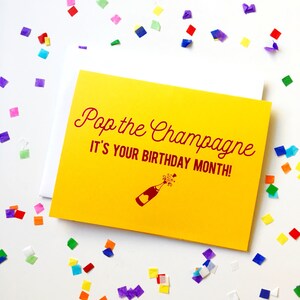 May include: Yellow card with the text "Pop the Champagne It's Your Birthday Month!" in red lettering. A red illustration of a champagne bottle with a cork popping is below the text.