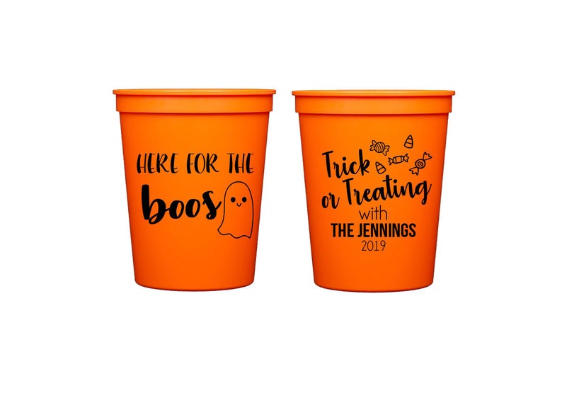 Pode incluir: Dois copos de pl&aacute;stico laranja com texto e gr&aacute;ficos pretos. Um copo diz "HERE FOR THE boos" com um fantasma. O outro diz "Trick or Treating with THE JENNINGS 2019" com gr&aacute;ficos de doces. Copos para festas de Halloween.