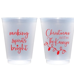 May include: Two white plastic cups with red text. One cup says "making spirits bright" with a star. The other cup says "Christmas with The Kaseys" with a string of lights.
