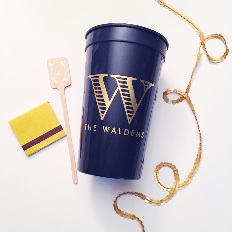 Puede incluir: Un vaso de pl&aacute;stico azul marino con una letra "W" dorada y el texto "The Waldens" impreso en el lateral. El vaso est&aacute; sobre una superficie blanca.
