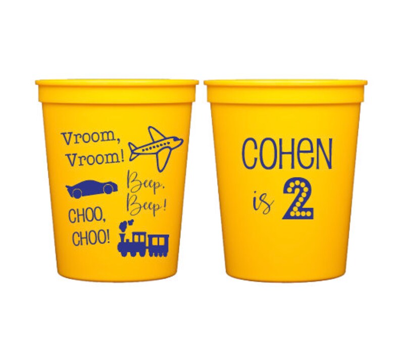 May include: Two yellow plastic cups with blue text. One cup says "Vroom, Vroom!" with a plane, car, and train. The other cup says "COHEN is 2" with a number 2.