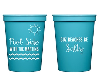 May include: Two turquoise blue plastic cups with white text. The left cup says "Pool Side with the Martins" and has a sun and waves design. The right cup says "Cuz Beaches Be Salty".