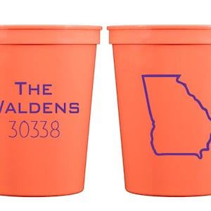 May include: Two orange plastic cups. One cup has the text "THE WALDENS 30338" printed on it. The other cup has an outline of the state of Georgia printed on it.