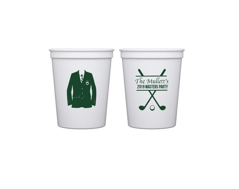 May include: Two white plastic cups. One cup features a green silhouette of a suit jacket and tie. The other cup has the text "The Mullett's 2019 Masters Party" above crossed golf clubs and a golf ball, all in green.