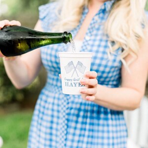 May include: A person pouring champagne into a white paper cup with a blue and white American flag design and the text "happy birthday HAYES".