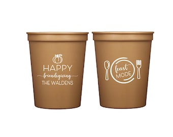 May include: Two brown plastic cups. One cup has a pumpkin graphic and the words "HAPPY friendsgiving THE WALDENS" in white. The other cup has a spoon, fork, and the words "feast MODE" in white.