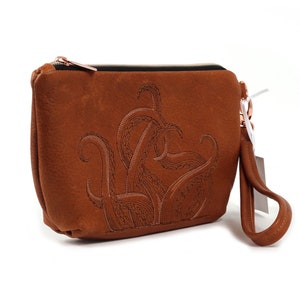 May include: A brown leather clutch bag with a zipper closure and a detachable wrist strap. The bag features an embroidered design of an octopus with tentacles.