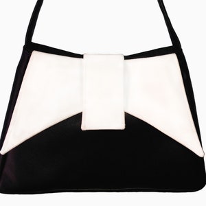 May include: A black leather handbag with a white bow detail. The bag has a single strap and a flap closure.