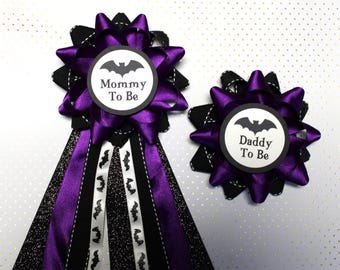 May include: Two purple and black bow sashes with a bat design and the text "Mommy To Be" and "Daddy To Be".