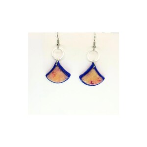 May include: A pair of handmade earrings with a fan-shaped design. The earrings feature a blue border with a light orange and pink interior. Each earring has a silver-colored circular accent and a hook for pierced ears.