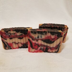 May include: Three bars of handmade soap with a red, black, and white swirl pattern. The soap is made with natural ingredients and is perfect for all skin types.