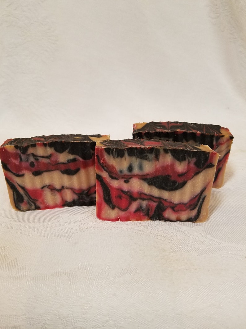 May include: Three bars of handmade soap with a red, black, and white swirl pattern. The soap is made with natural ingredients and is perfect for all skin types.